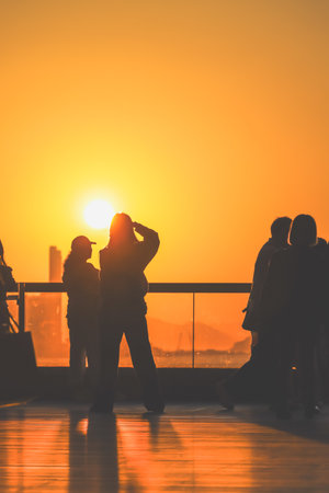 figures stand by a glass railing as a brilliant orange sunset Nov 16 2025のeditorial素材