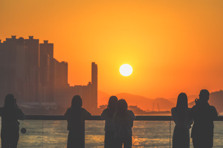 Silhouetted group stands on a sunlit balcony as the city skyline glows Nov 16 2025のeditorial素材