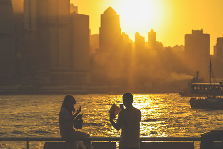 Two silhouetted figures by a railing overlook a golden sunset Nov 16 2025のeditorial素材