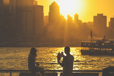 Two silhouetted figures by a railing overlook a golden sunset Nov 16 2025のeditorial素材