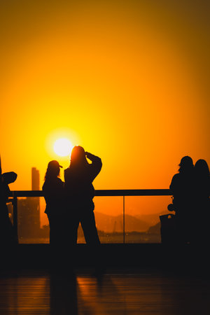 figures stand by a glass railing as a brilliant orange sunset Nov 16 2025のeditorial素材