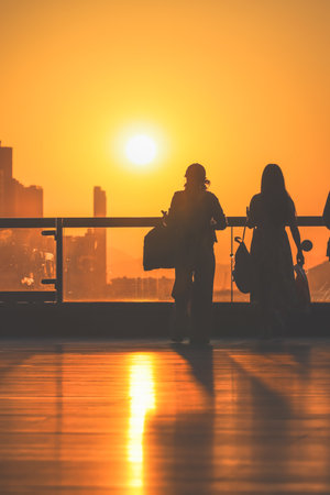 figures stand by a glass railing as a brilliant orange sunset Nov 16 2025のeditorial素材