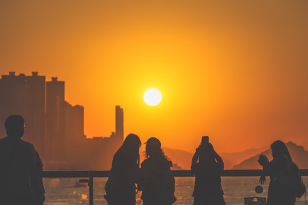 figures stand by a glass railing as a brilliant orange sunset Nov 16 2025のeditorial素材