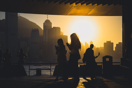 figures stand by a glass railing as a brilliant orange sunset Nov 16 2025のeditorial素材