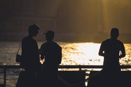 Silhouetted figures stand along a railing at sunset, overlooking a shimmering Nov 16 2025のeditorial素材