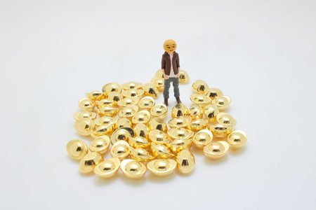 Tiny model figure poses peacefully atop reflective gold piecesの写真素材