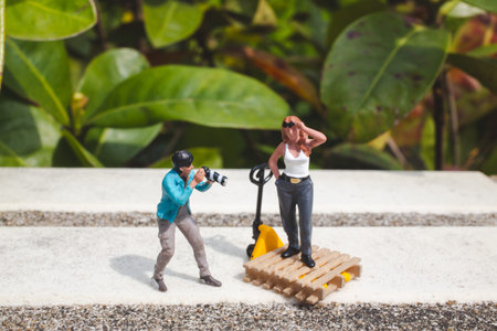 Tiny figurines recreate photo shoot setup beside green leafy backdropの写真素材