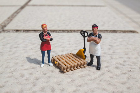Miniature workers stand beside pallet and yellow hand truck