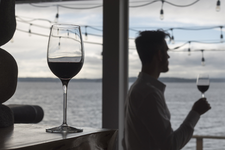 Hero red wine on mantel with silhouetted man holding glass in the backgroundの写真素材