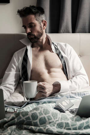 Professional handsome man in bed with coffee workingの写真素材