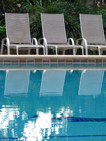 empty chaise lounge chairs reflecting in poolの写真素材