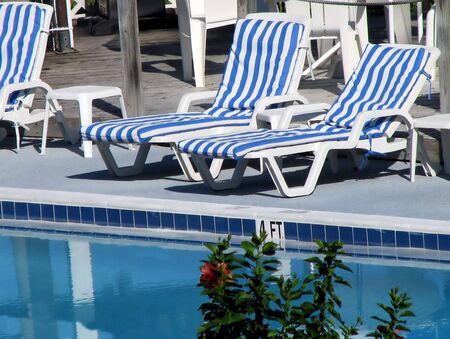 empty chaise lounge chairs reflecting in pool