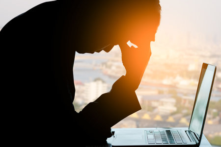 A man sitting down, his face unsettled. At the computer desk he has headaches and stress. Cause of hard work and insufficient rest.の写真素材