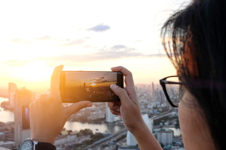 Asian woman take pictures of the buildings in the city. Sunrise time He uses a high-angle recording photo phone.Travel concepts and technologyの写真素材