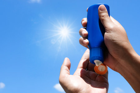 Hand of female holding sunscreen. Very sun light Sky background.Health concepts and skin care