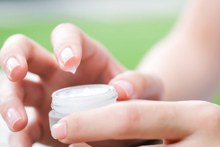 Hand of woman holding moisturizer cream and serum. She applying a facial cream , essential , oil , lotion and body cream for skin care, close up view and blur background. Beauty and Healthy Concept.の写真素材