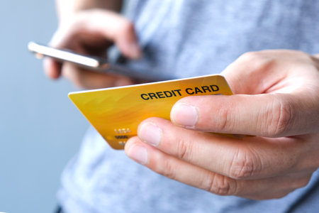 Young man sat in the living room on the sofa holding his credit card.の写真素材