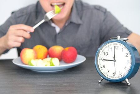 Ancient clock . Black ground young man eating fruit, fiber and dietary fiber. healthy food conceptの写真素材