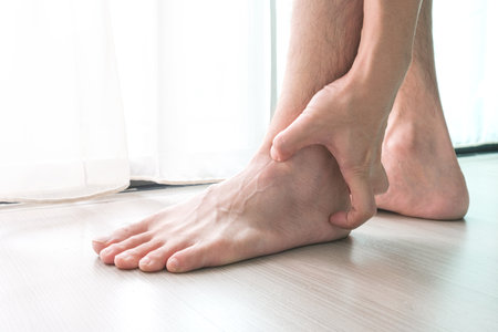 Ankle Pain man sitting on wooden background holding her feet. Health concept.の写真素材