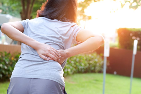 Woman's hand She is caught at the waist and her back is painful at the back in the park. Cause of the exercise.の写真素材