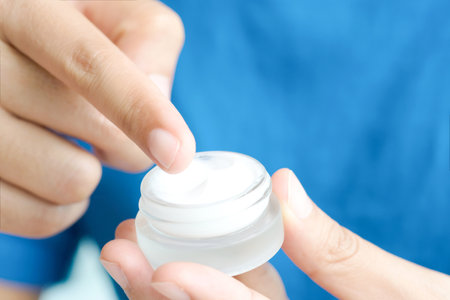 Hand of woman holding moisturizer cream and serum. She applying a facial cream , essential , oil , lotion and body cream for skin care, close up view and blur background. Beauty and Healthy Concept.の写真素材