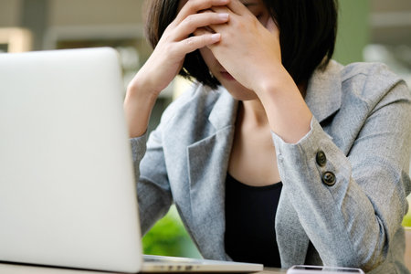 A man sitting down, his face unsettled. At the computer desk He has headaches and stress. Cause of hard work and insufficient rest.の写真素材