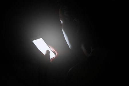 woman does not sleep and is stressed at night. She uses and looks smartphone in the bedroom without light and darkness.の写真素材