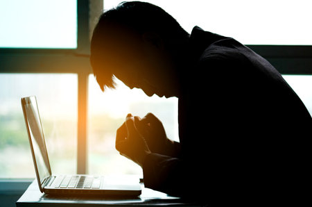 Man sitting down, his face unsettled. At the computer desk she has headaches and stress. Cause of hard work and insufficient rest.の写真素材