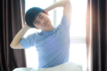 Morning of a new day, alarm clock wake up man sitting in the room. A woman stretch the muscles at...