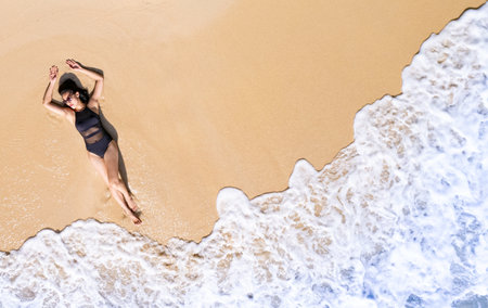 Aerial view, women lounging, sunbathing on the beach and beautiful blue water waves on the island of...