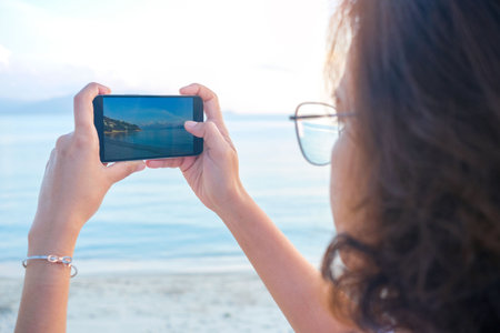 Woman taking pictures of beach, sea and resort at sunrise He used his phone to take high-angle...