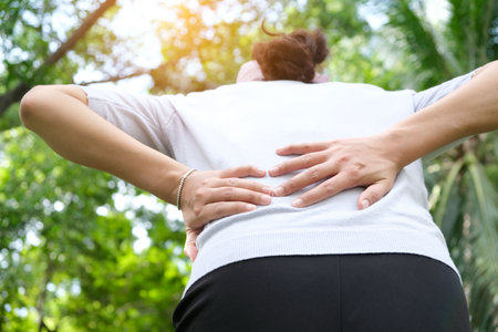 Woman's hand She is caught at the waist and her back is painful at the back in the park. Cause of the exercise.の写真素材