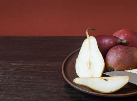 Ripe organic red and yellow pears and slices of pears in a clay bowl with knife on a dark wooden background. Fresh pear closeup. Background with yellow and red pears top view. High quality photoの写真素材