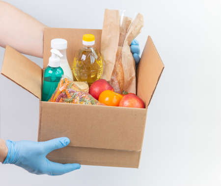 Person in latex gloves has holding a box with ordered goods. Safe food delivery service under quarantine. Online food shopping service or donation concept. White background.High quality close-up photoの写真素材