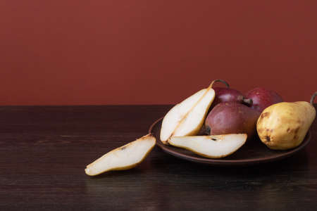 Ripe organic red and yellow pears and slices of pears in a clay bowl on a dark wooden background....