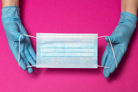 Hands in blue medical gloves is holding face mask on pink background. Protective respiratory medical...