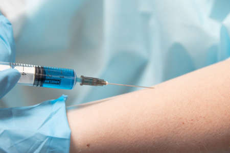 Doctor in medical latex gloves injects flu, measles, coronavirus covid-19 vaccine. Syringe and...