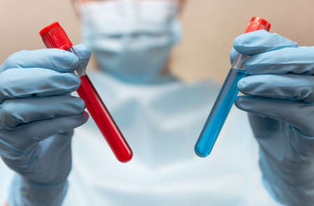 Doctor in protective suit, medical mask and latex gloves holds a test tubes with blood and vaccine....