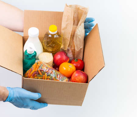 Person in latex gloves has holding a box with ordered goods. Safe food delivery service under quarantine. Online shopping food service or donation concept.White background.High quality close up photoの写真素材