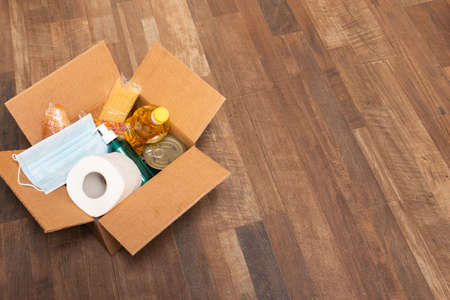Donation goods in carton box on the floor. Pasta, toilet paper, medical mask, sunflower oil, sanitizer, caned food, bread. Food delivery for those who need.の写真素材