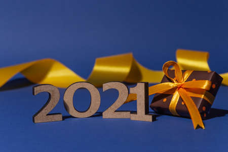 Inscription 2021, decorative ribbon and gift box with color paper with polka dots tied yellow ribbon on blue background. Christmas and New Year card, banner, advertising concept. High quality photoの写真素材