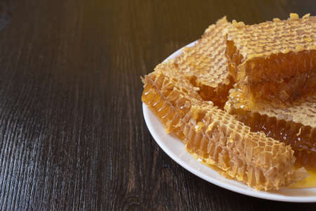 Honeycombs in white plate on the wooden table. Natural organic bee product. Healthy lifestyle. Copy space for your text. Close-up photo.の写真素材