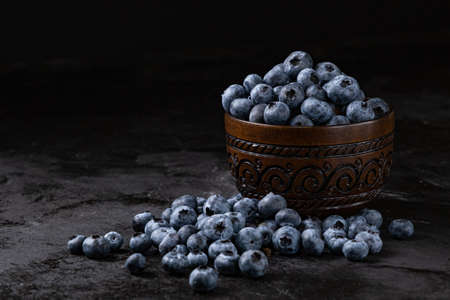 Fresh juicy blueberries in the bowl on the black background. Low key photographyの写真素材