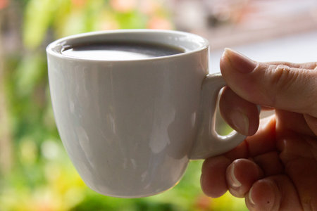 Hand holding a cup of coffee on the background of green garden.の写真素材