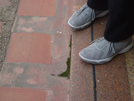 Close up of a man's feet wearing white sneakers on a pavementの写真素材