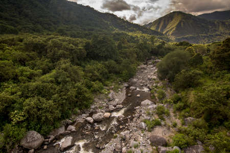 Smooth waters in a mountain river going down from with a lot of wild vegetation and gray rocks on a cloudy day. Catamarca Province, Argentina.の写真素材
