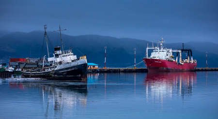 Old black ship and new red ship anchored in Beagle Channel waters in Ushuaia, Tierra del Fuego, Argentina. In the background little mountains that belongs to Andes Mountain range, South frontier.のeditorial素材