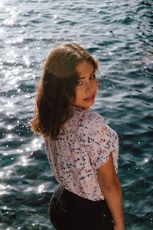 Girl in front of the sea smiling at camera, with brown hair and Latin roots. Clear turquoise blue sea, near the rocky coast of Mallorca.の写真素材