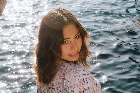 Girl in front of the sea smiling at camera, with brown hair and Latin roots. Clear turquoise blue...