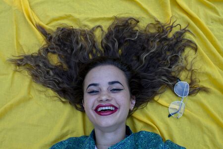 Vertical side profile top above high angle photo beautiful she her lady lying down show perfect shiny ideal hair above head slim skinny wearing formal wear yellow cloth background backgroundの写真素材